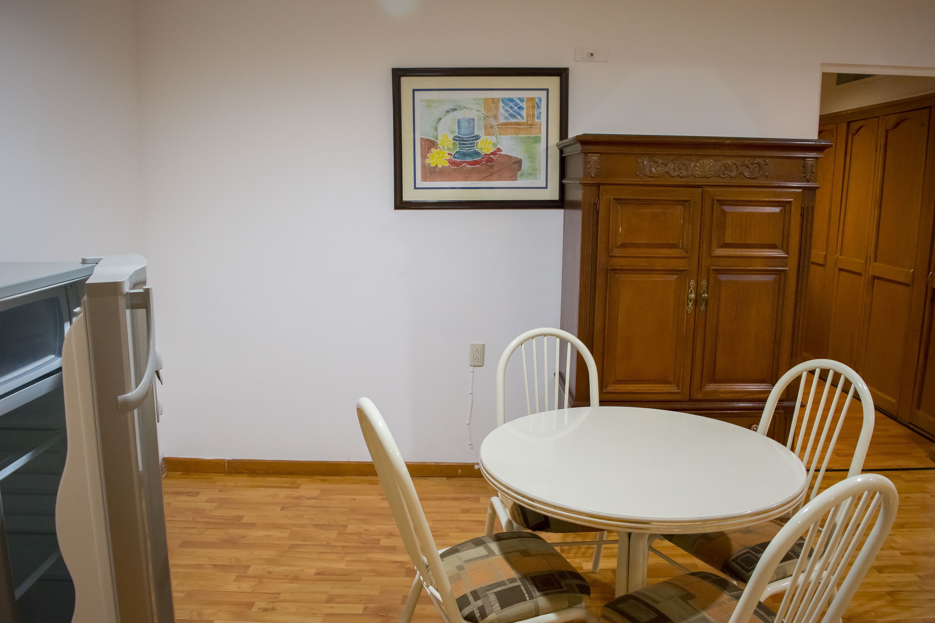 Un comedor con una mesa redonda y cuatro sillas, un armario de madera y un cuadro en la pared.