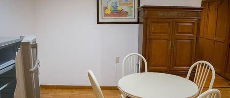 Un comedor con una mesa redonda y cuatro sillas, un armario de madera y un cuadro en la pared.