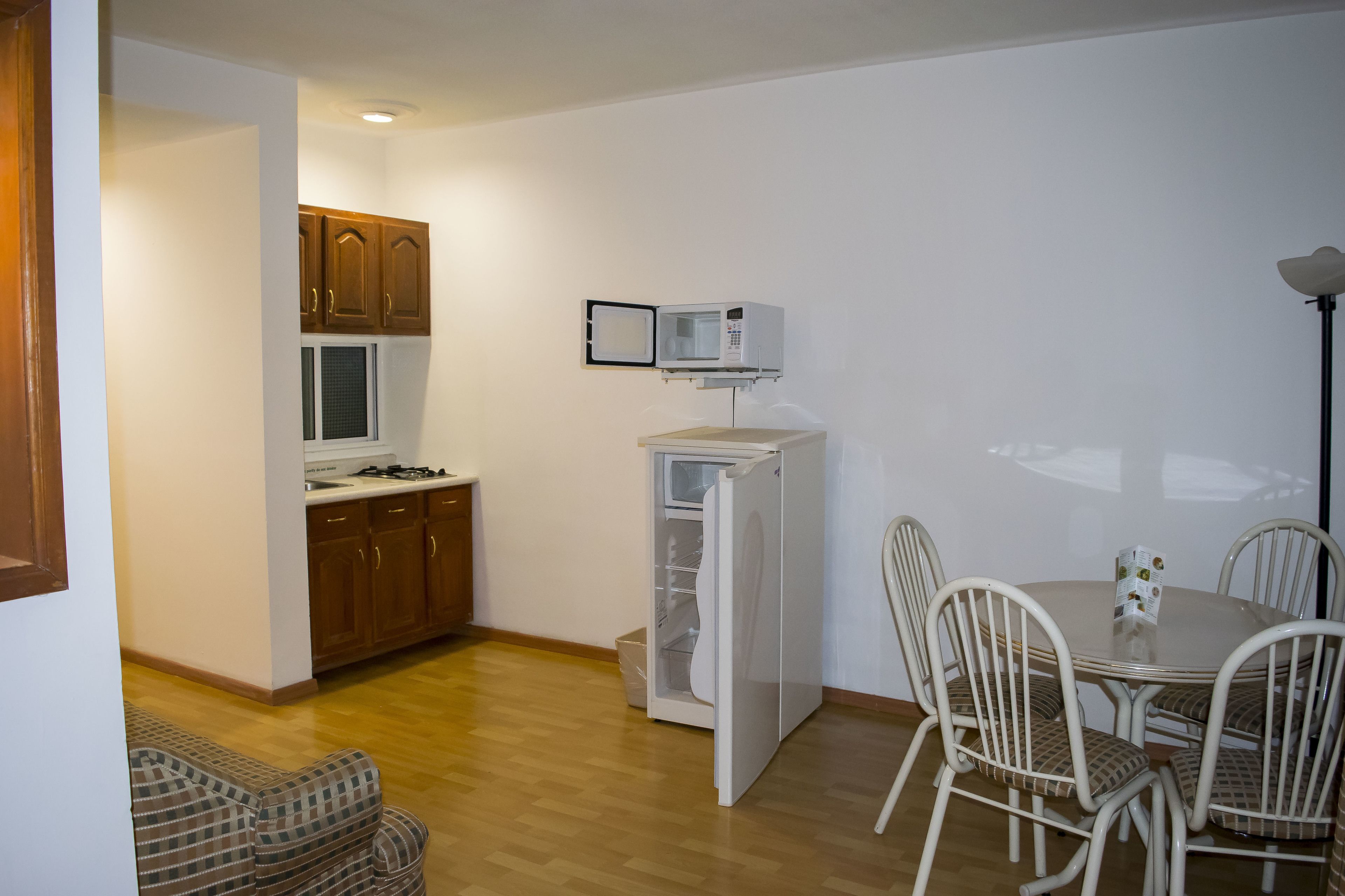 A compact kitchen with wooden cabinets, a microwave, and a refrigerator. There is a dining table with chairs and a small sofa.