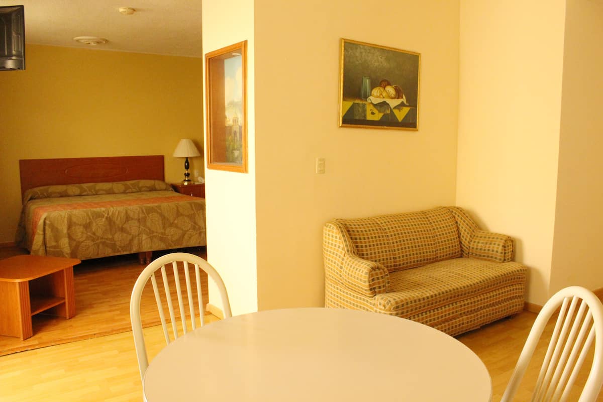 A hotel room with a bed, a sofa, a dining table, and a painting on the wall.