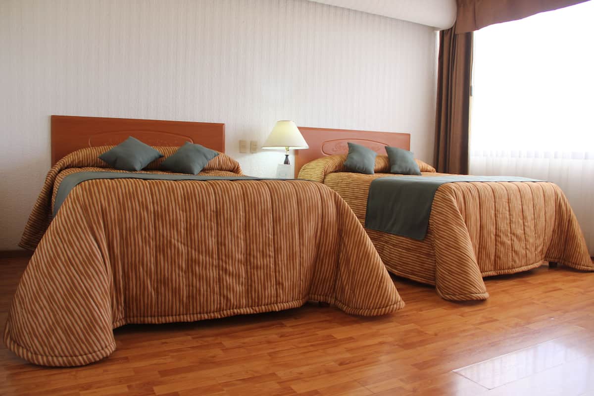 Two beds with striped bedding, a nightstand with a lamp, and a window with curtains.