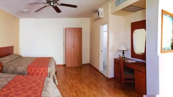 A hotel room with two beds, a desk, a chair, a mirror, and a ceiling fan.