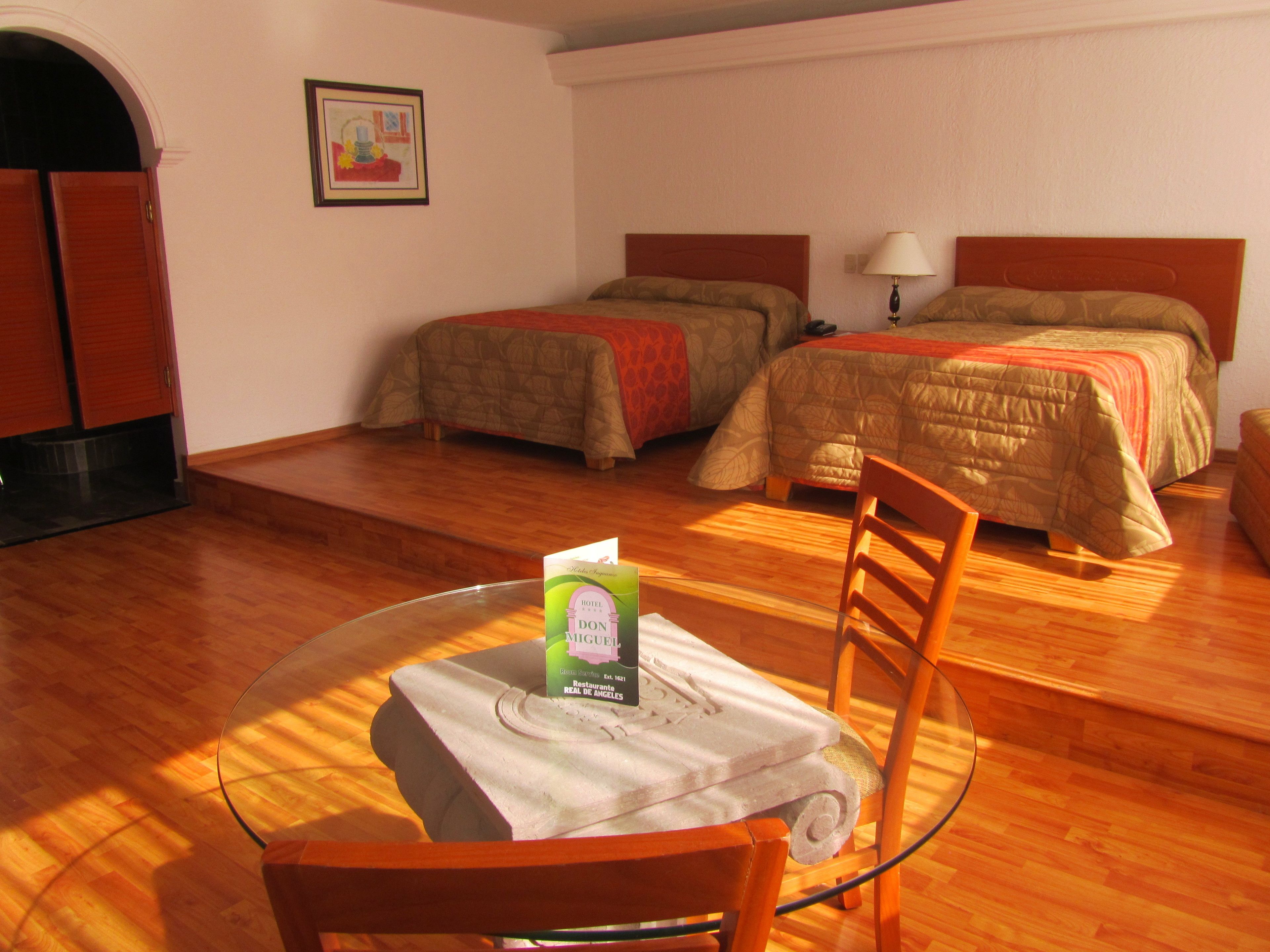 A hotel room with two beds, a dining table with a chair, and a framed picture on the wall.