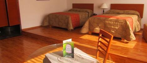 A hotel room with two beds, a dining table with a chair, and a framed picture on the wall.