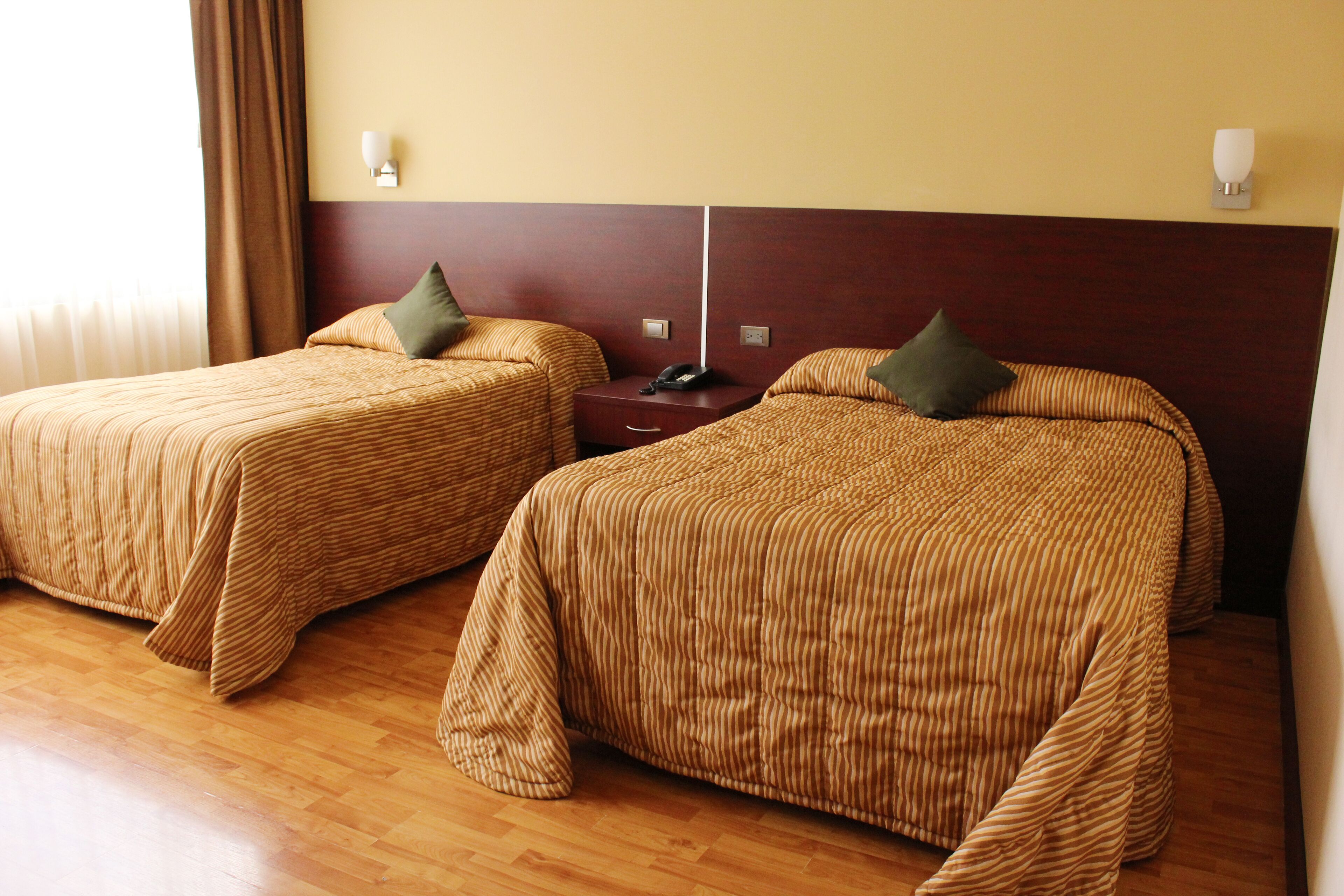 Dos camas individuales con ropa de cama a rayas, piso de madera y una mesita de noche con teléfono.