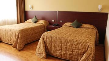 Dos camas individuales con ropa de cama a rayas, piso de madera y una mesita de noche con teléfono.