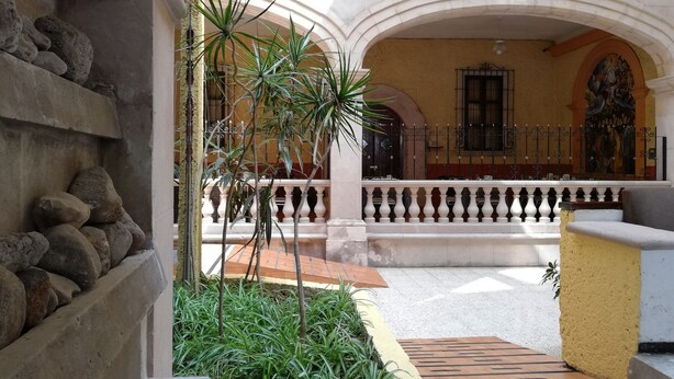 A courtyard with a stone wall, a metal railing, and a tiled floor. - Hotel María Benita (Zacatecas)