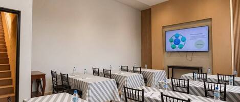 Un salón de conferencias con mesas, sillas, una pantalla de proyector y una escalera.