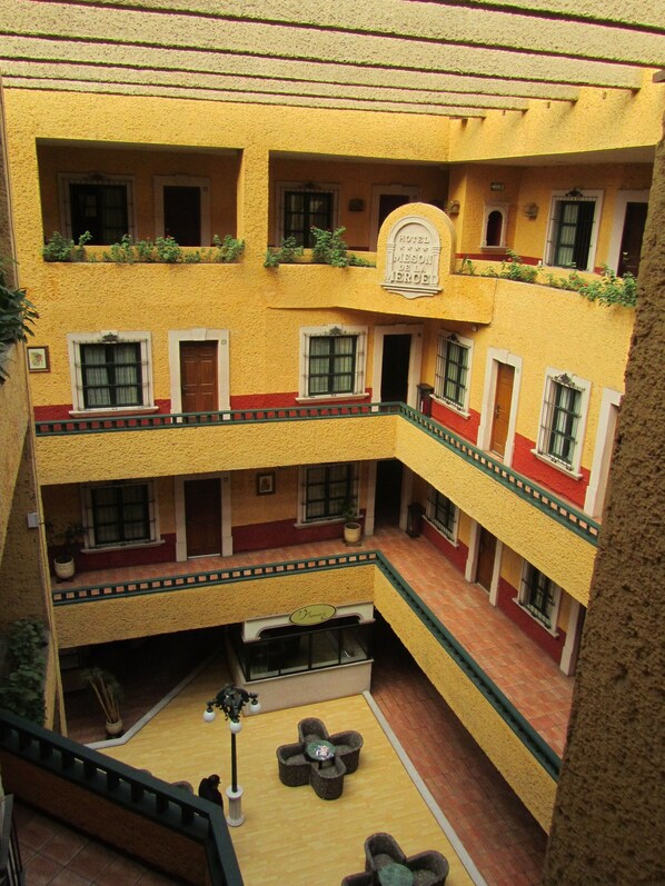 A multi-story hotel with a yellow facade, balconies with plants, and a central courtyard with seating. - Hotel Mesón de la Merced (Zacatecas)