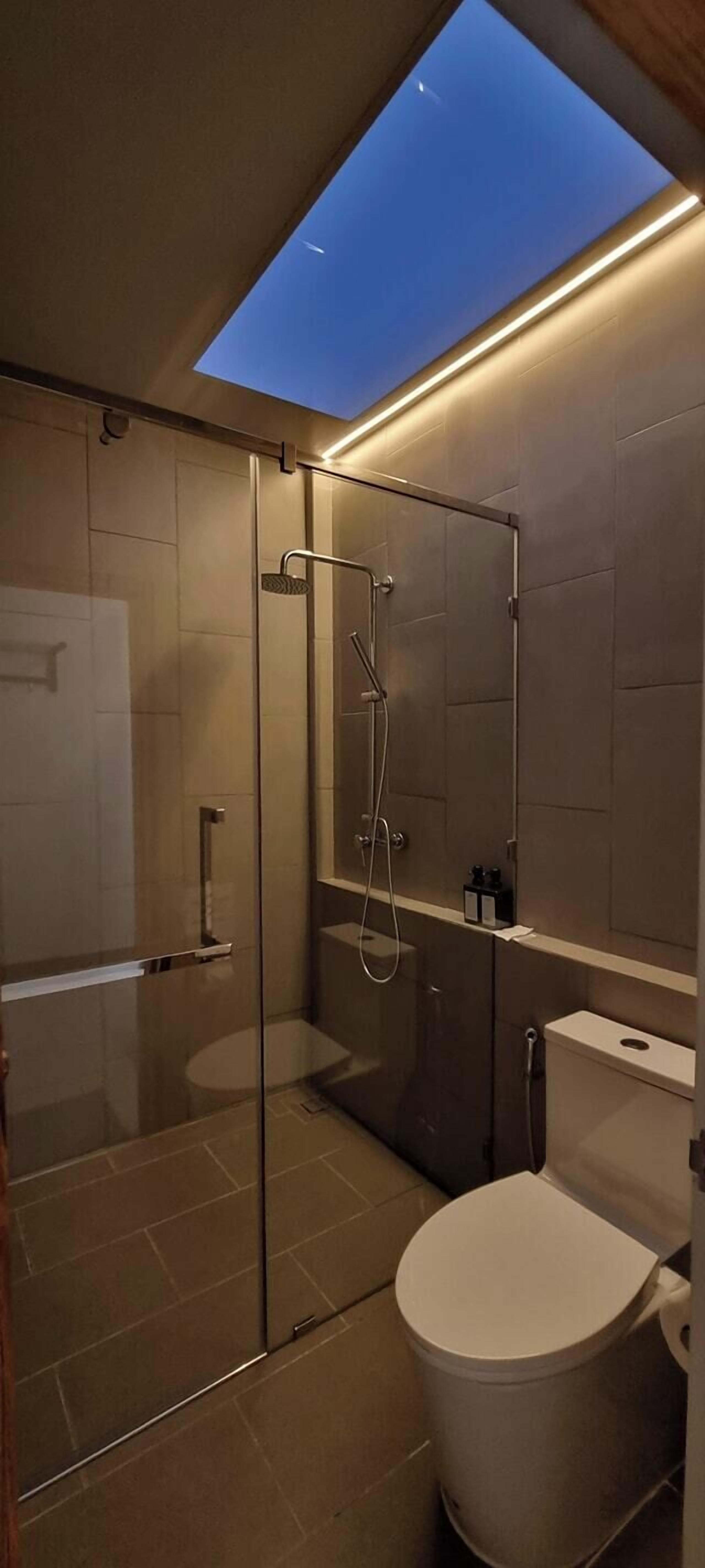 Un baño moderno con tragaluz, cabina de ducha de vidrio y un inodoro blanco.