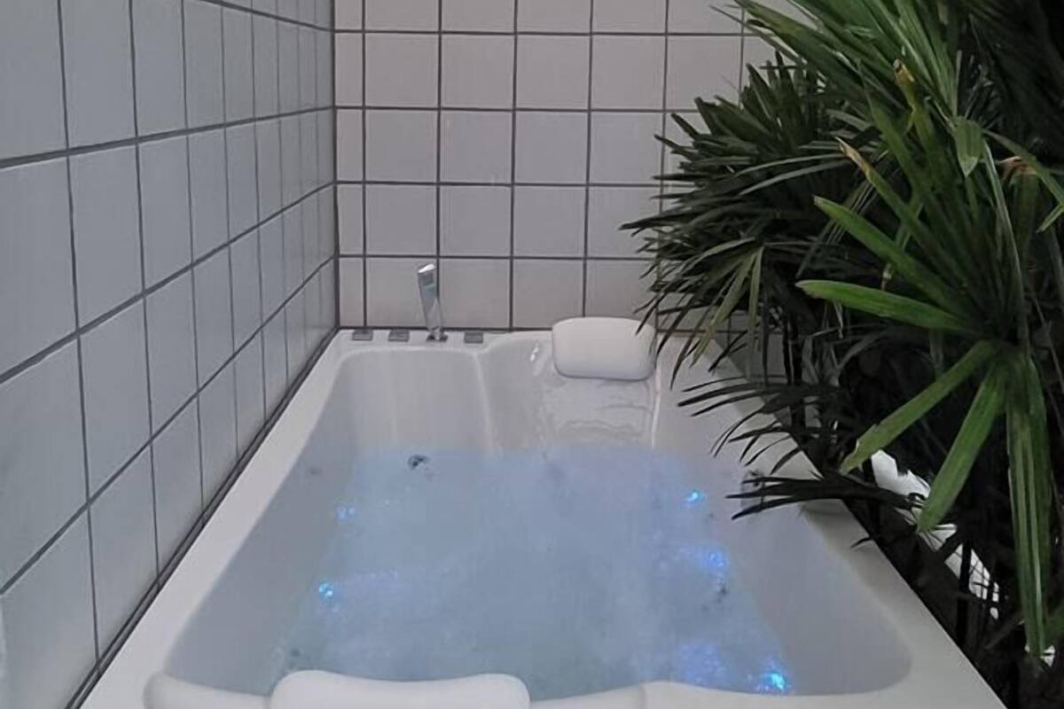 A modern bathroom with a white bathtub, tiled walls, and a wooden bench.