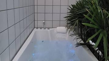A modern bathroom with a white bathtub, tiled walls, and a wooden bench.