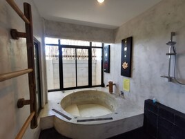 Un baño con una bañera independiente, una escalera de madera, ducha y ventana con vista a una cerca.