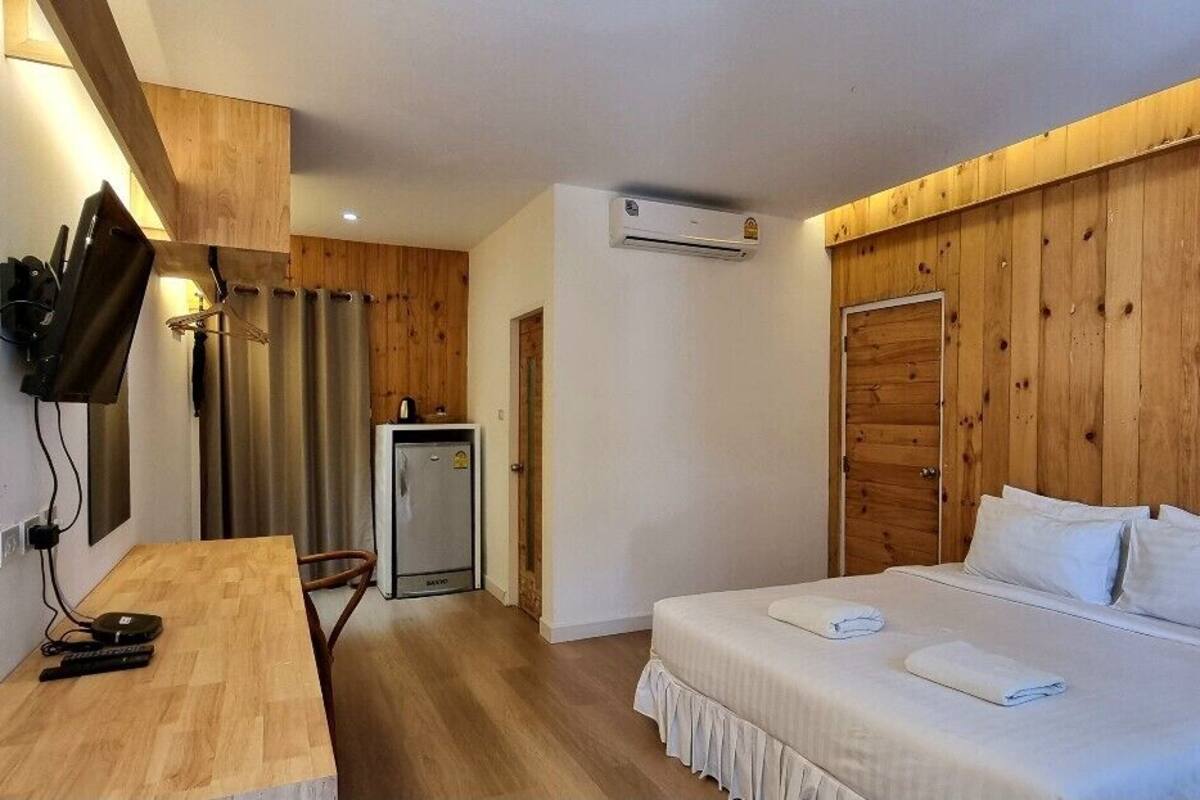 A hotel room with a wooden wall panel, a bed with white linens, a desk with a computer, and an air conditioning unit.