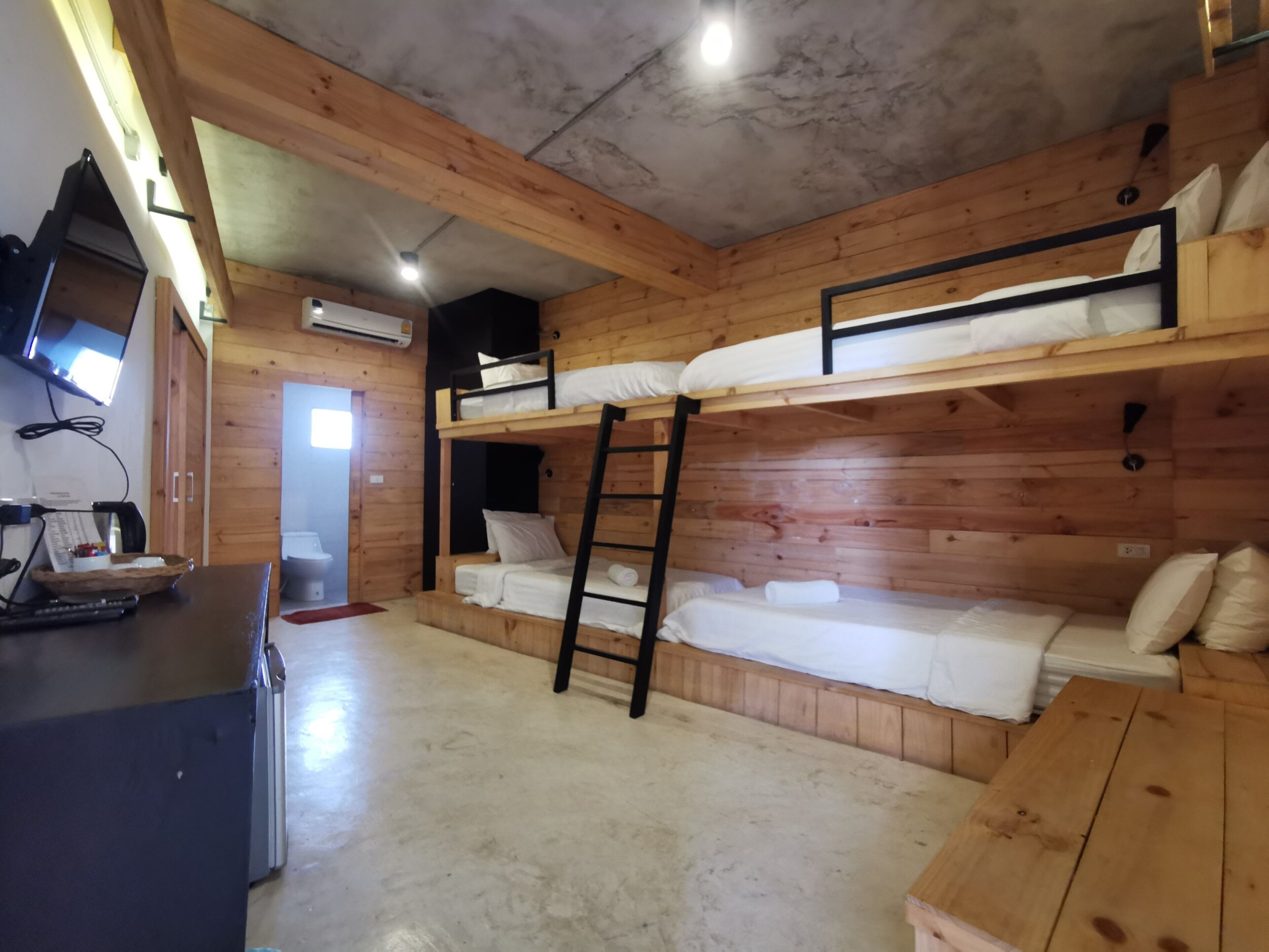 A bunk bed room with wooden walls, a desk with a computer, and a TV mounted on the wall.