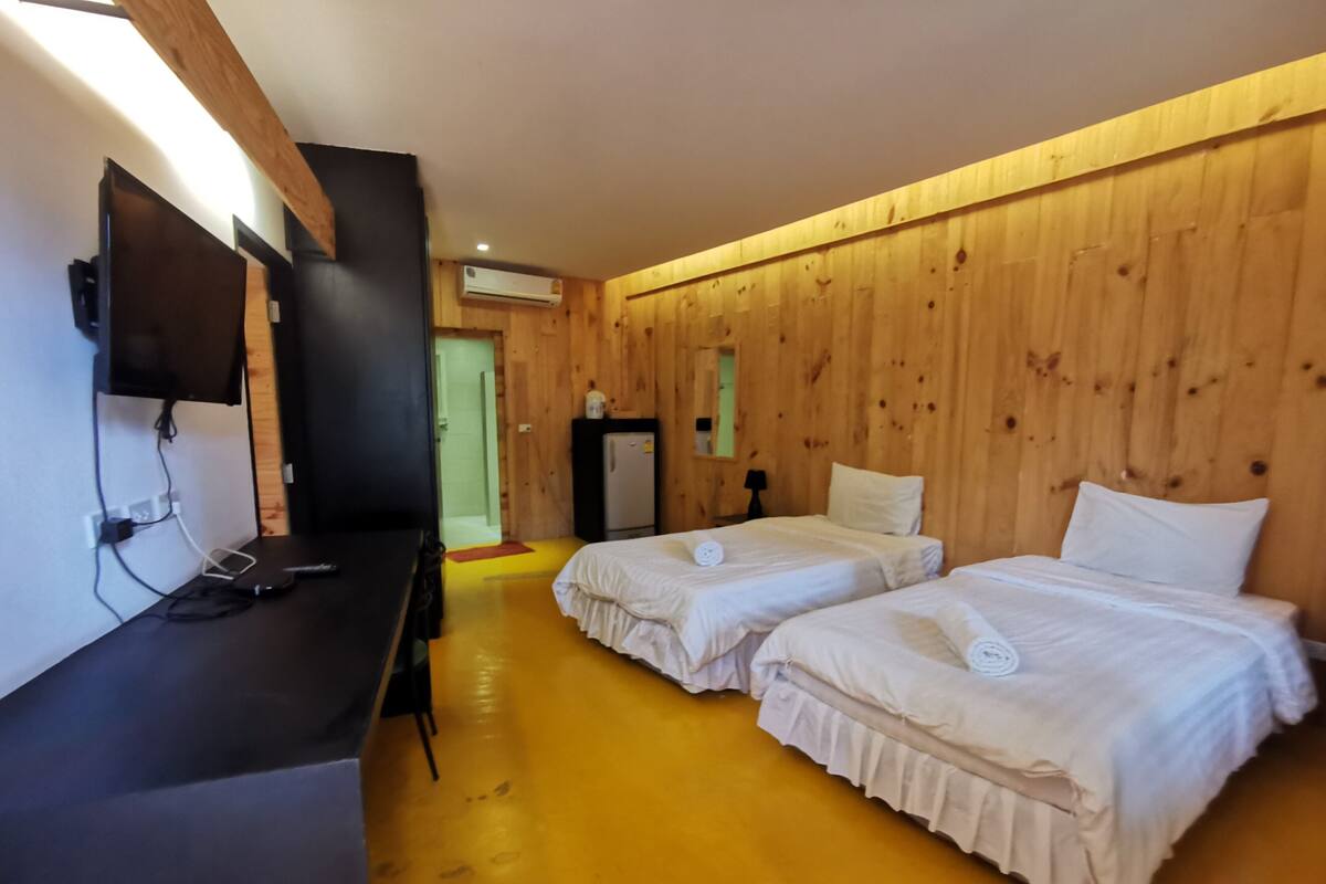 A room with two beds, a desk with a computer, a TV, and an air conditioning unit.