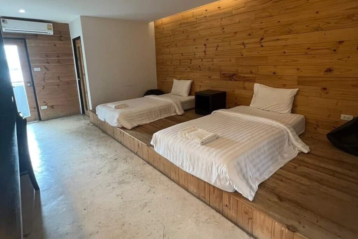 A room with two beds against a wooden wall, a small table, and a door.