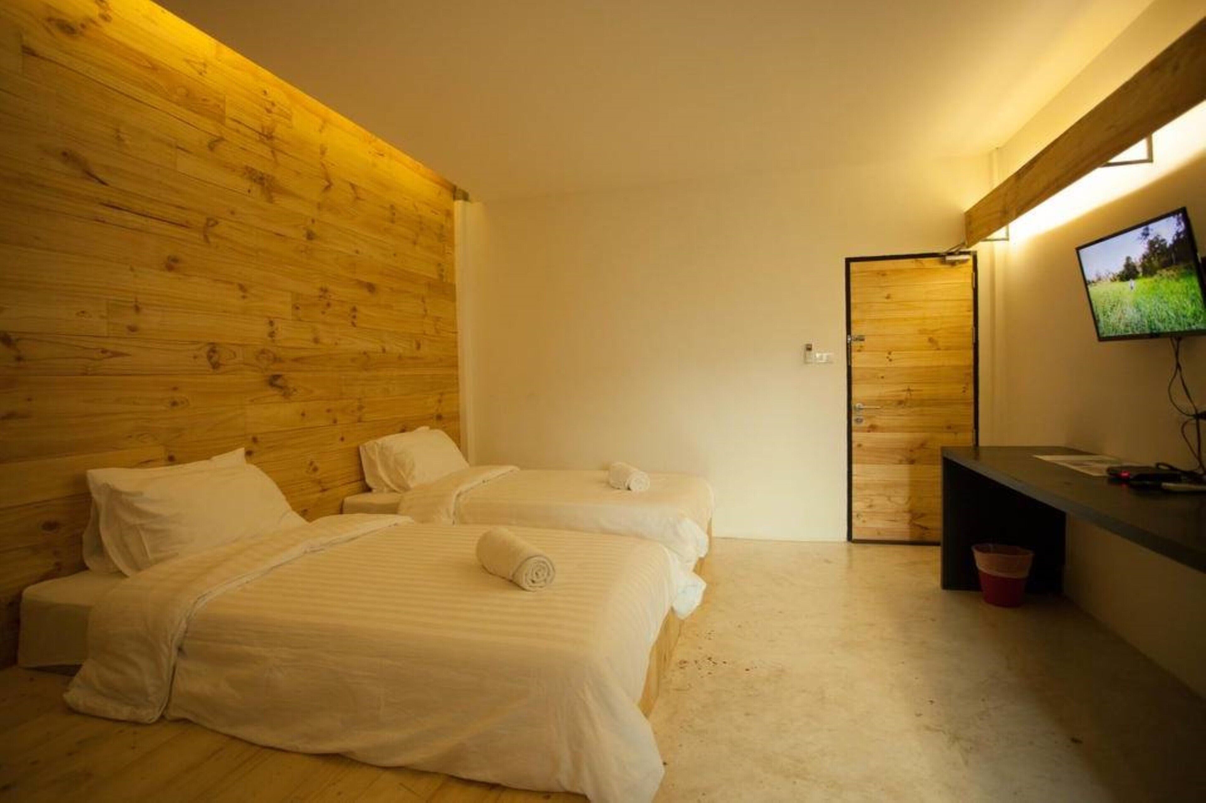 A room with two beds, wooden paneling on the walls, a television on the right, and a wooden door.