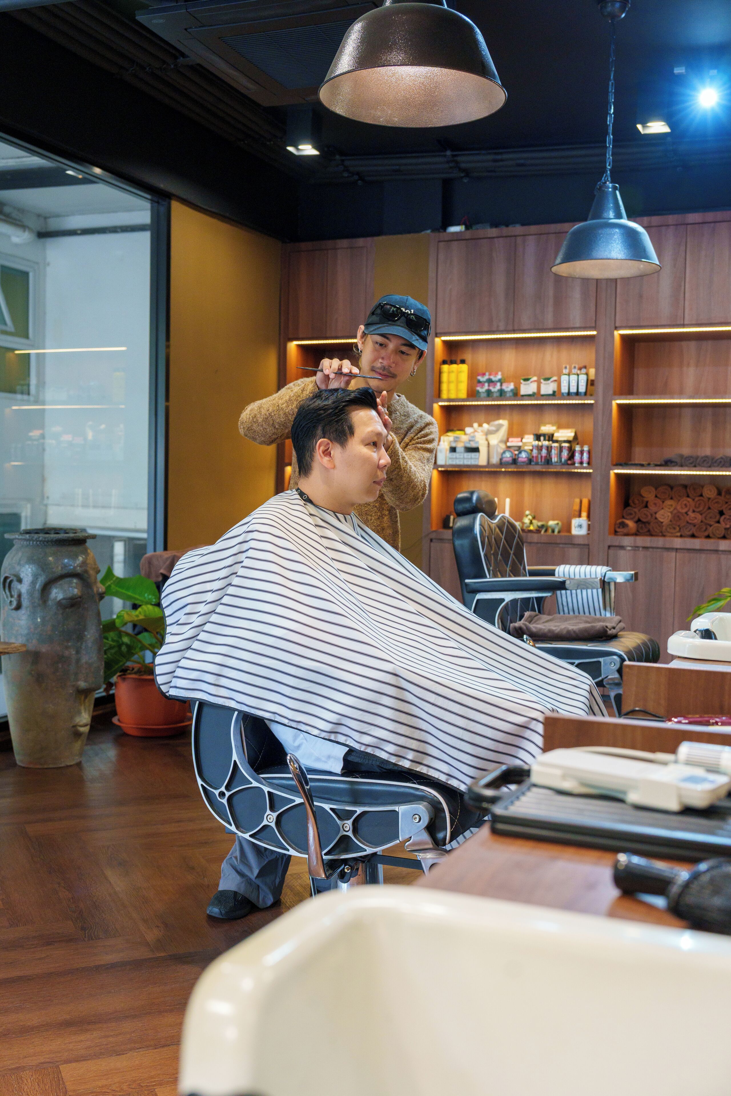 A barber shop interior with a wooden floor, a barber chair, a shelf with various items, and a hanging light fixture.