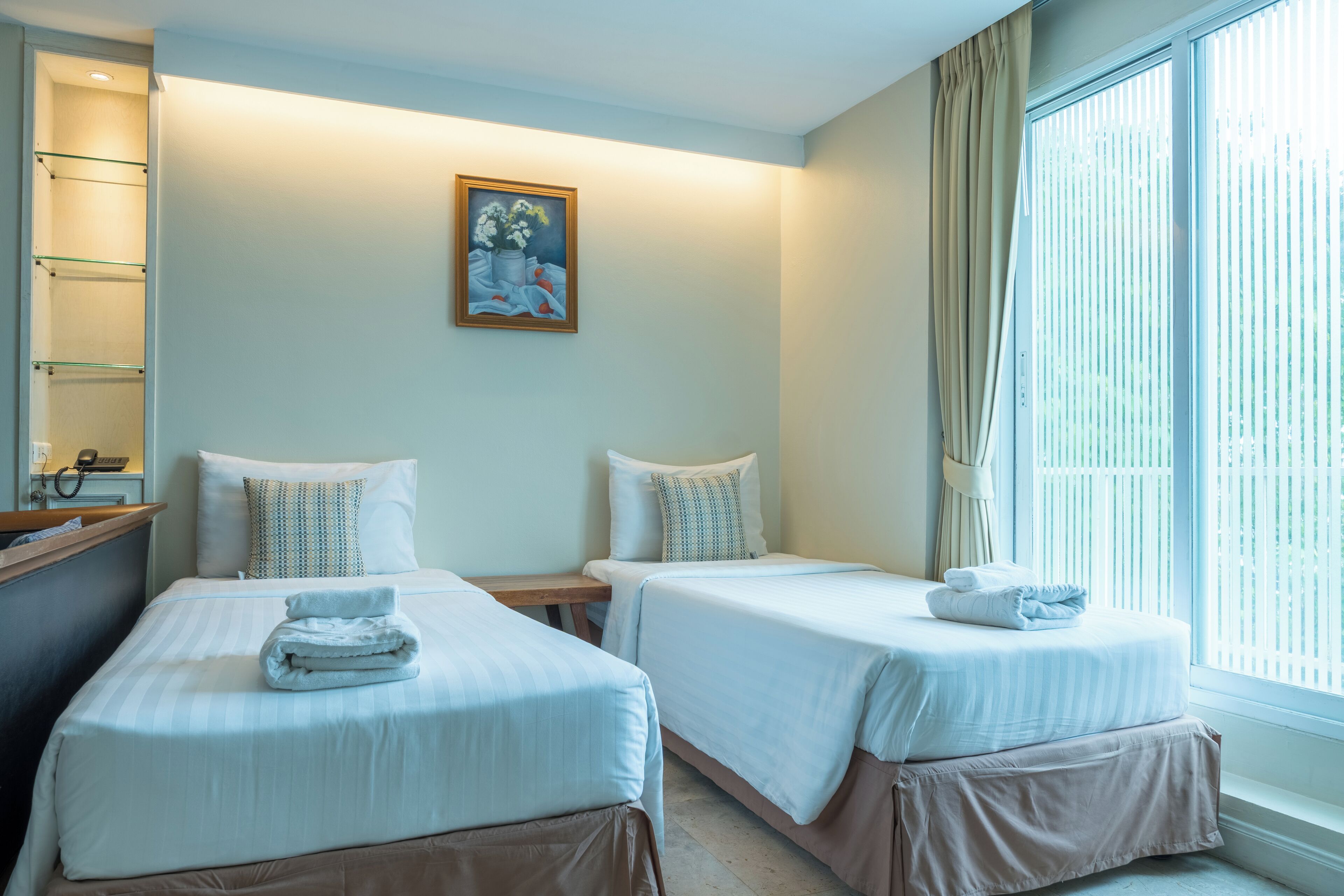 A hotel room with two beds, a painting on the wall, and a window with curtains.