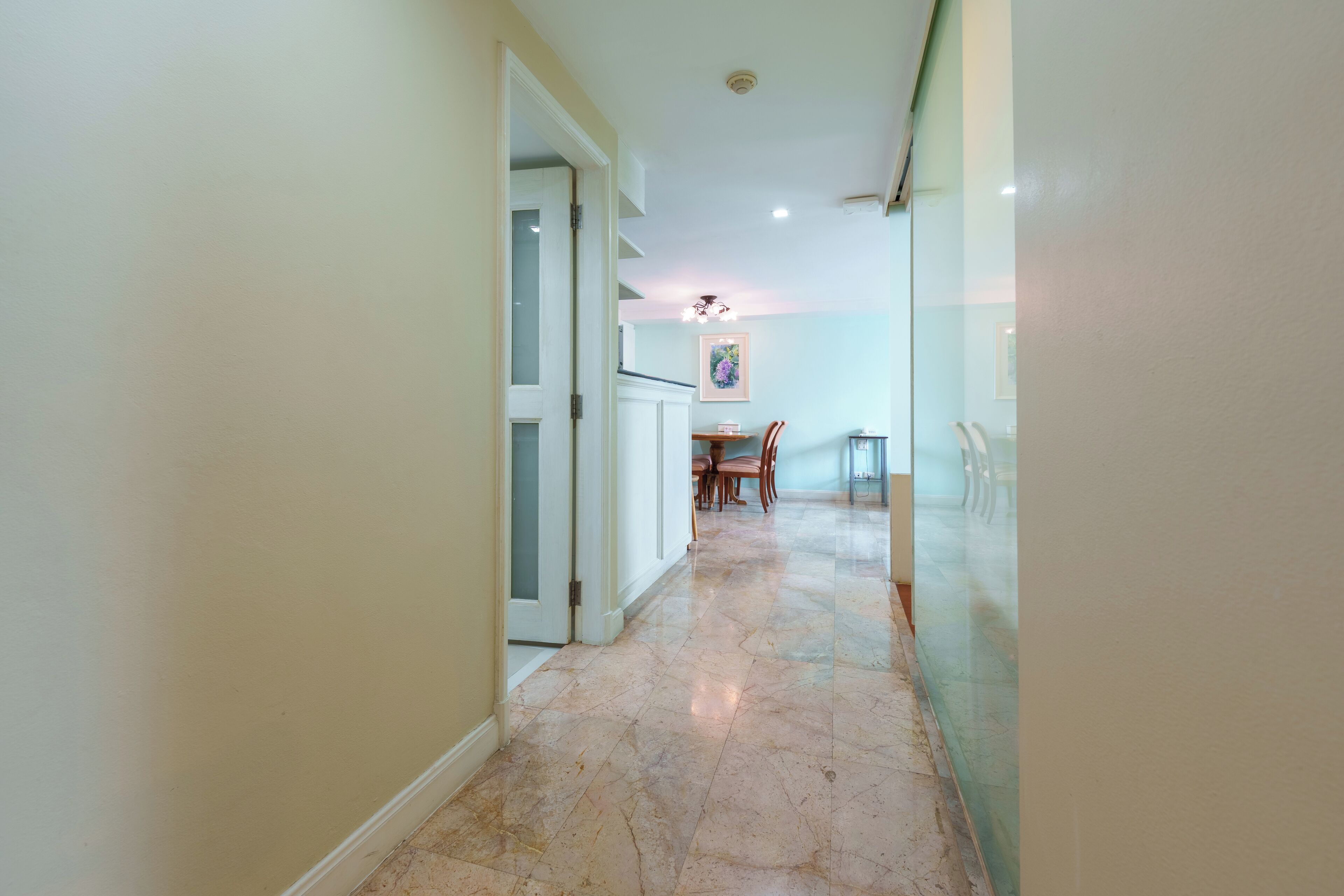 A hallway with a marble floor leading to a dining area with a table and chairs.