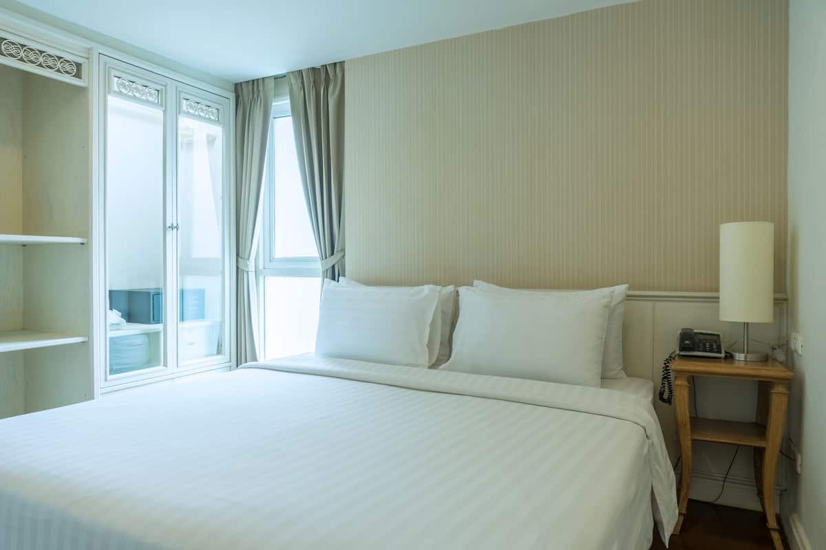 A hotel room with a large bed, a bedside table with a lamp, a telephone, and a wardrobe.