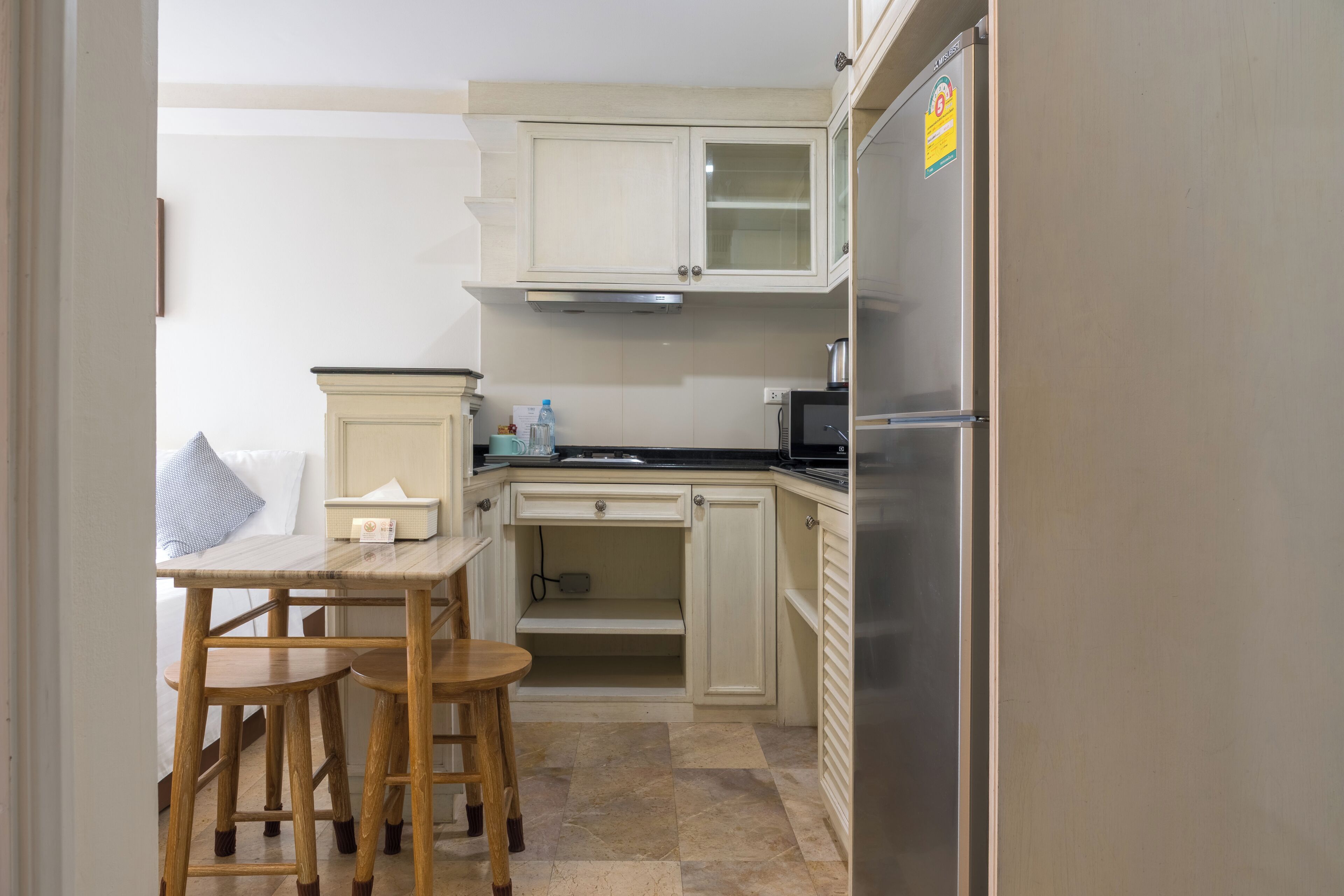 Eine kompakte Küchenzeile mit Kühlschrank, Mikrowelle und einer kleinen Essecke mit Hocker.