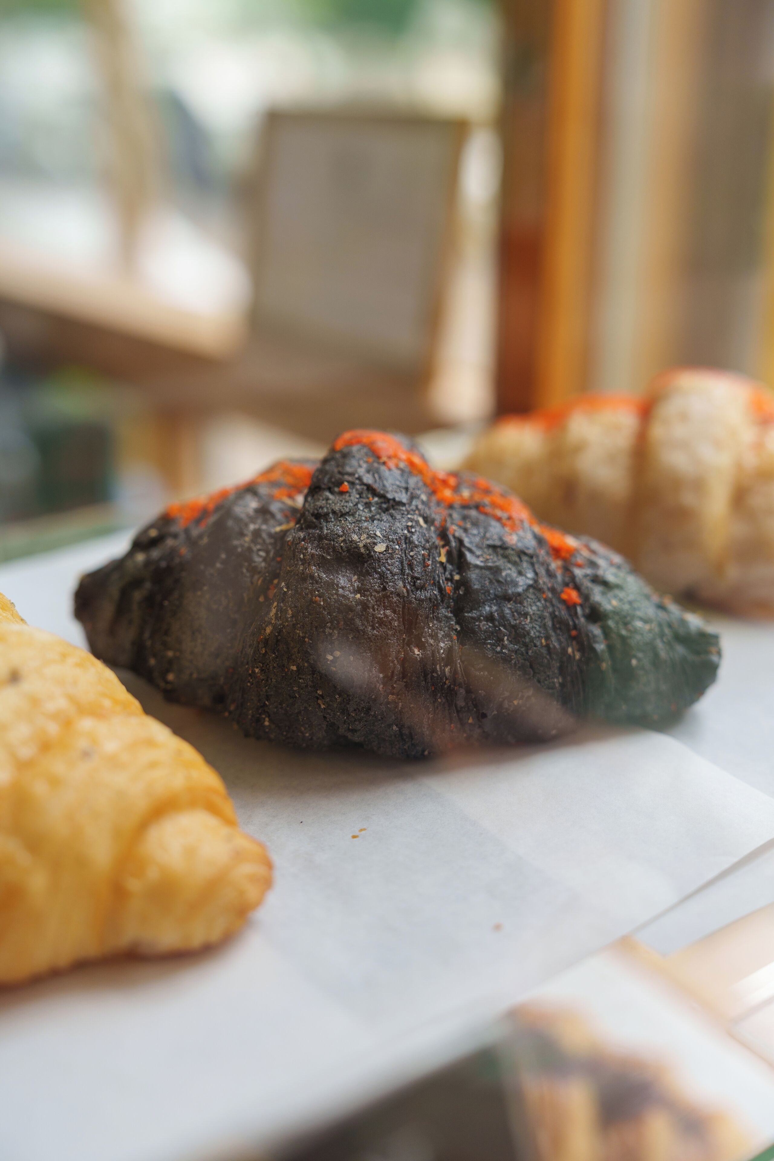 Primer plano de un alimento con superficie oscura y texturizada, cubierto de condimento anaranjado, posiblemente pan o una pieza de repostería, sobre un plato blanco.