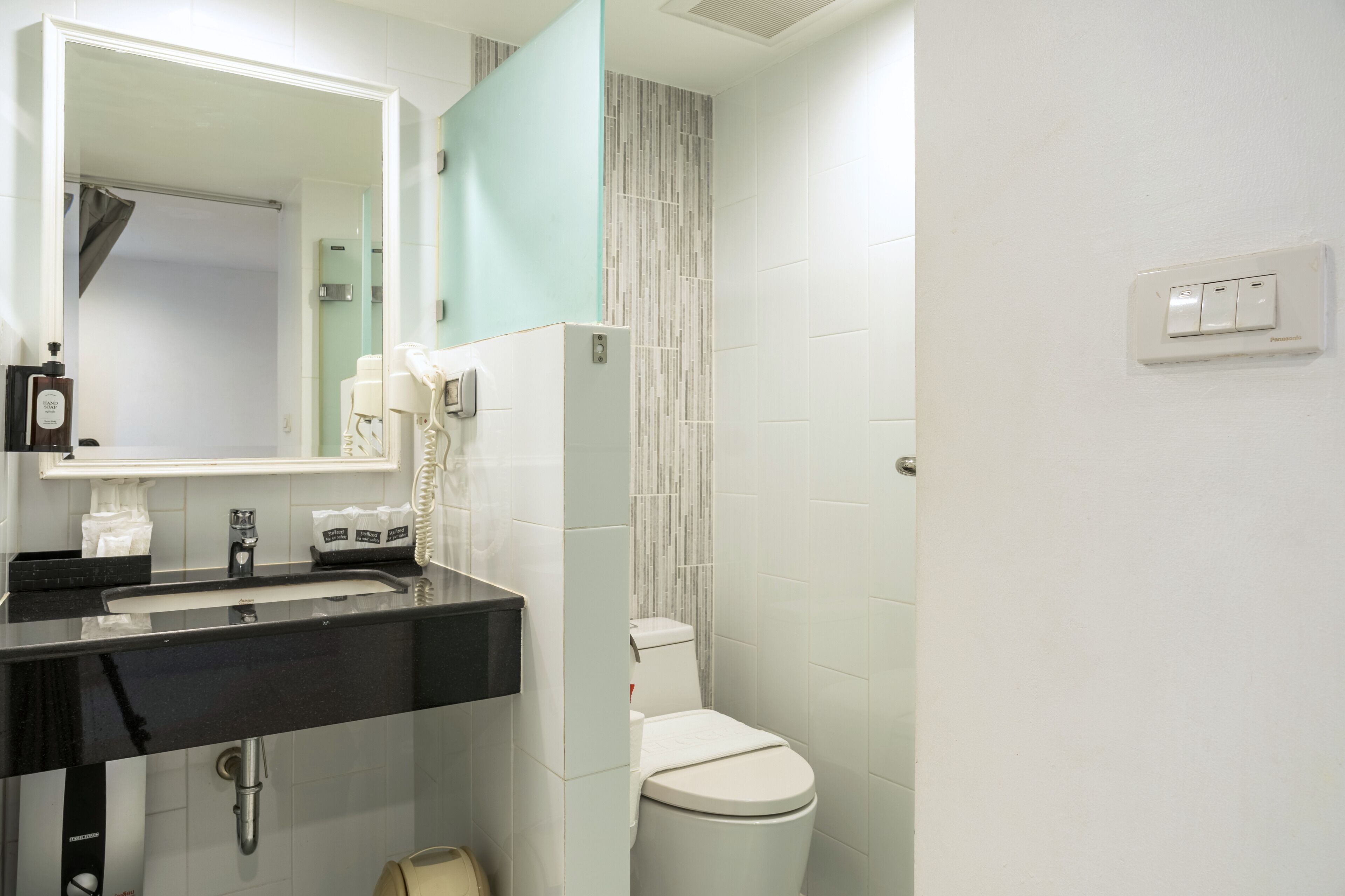 Un baño moderno con un lavabo negro, inodoro blanco y un espejo con detalles verde azulado.