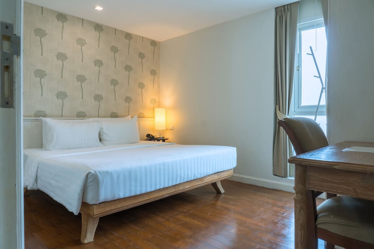A bedroom with a bed, bedside table, lamp, and a window with curtains.