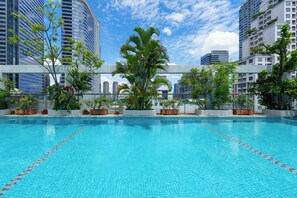 Una piscina azul cristalina con vistas a altos edificios y exuberante vegetación.