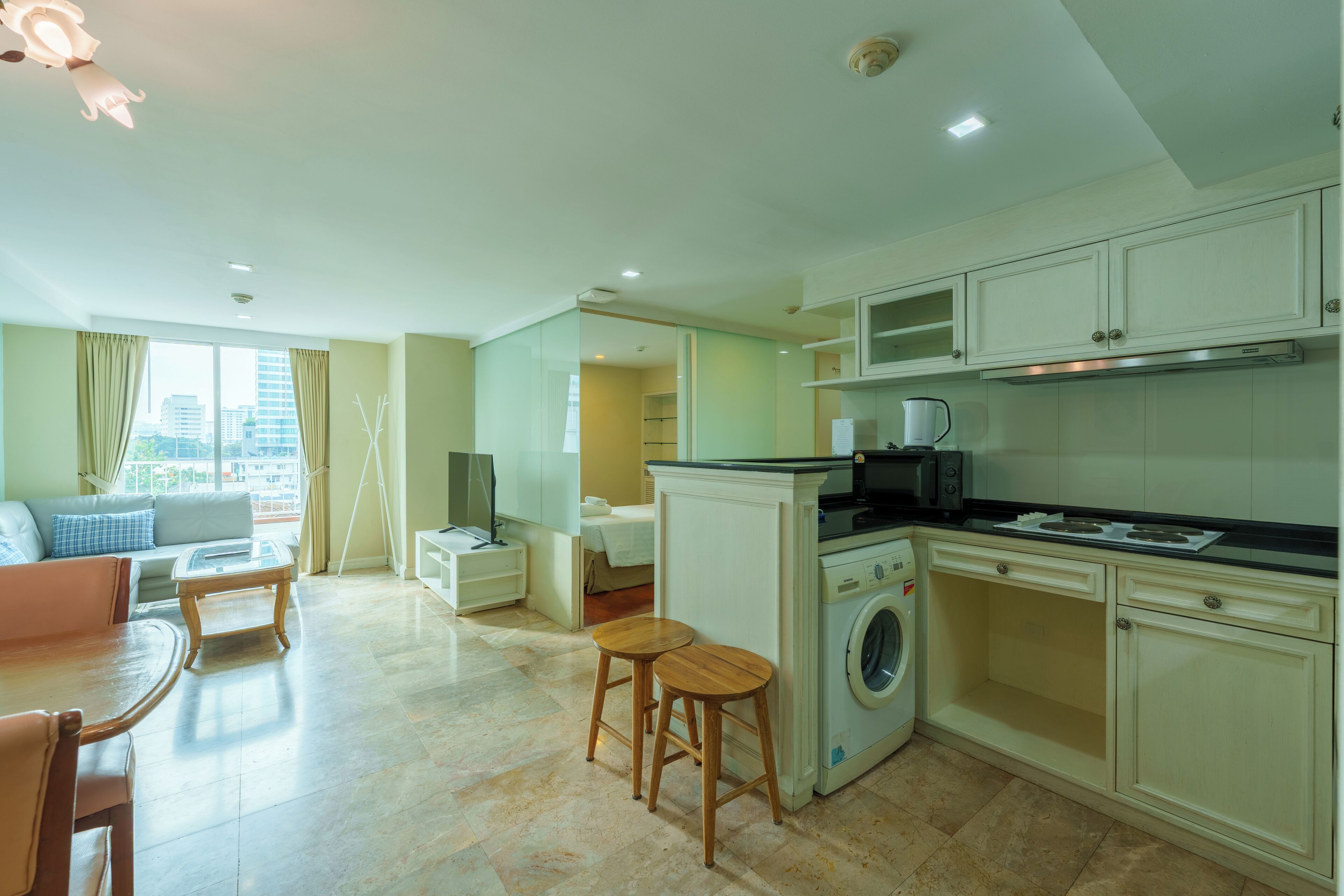 A modern apartment with a living room, kitchen, and laundry area. It includes a sofa, dining table, kitchen appliances, and a washing machine.