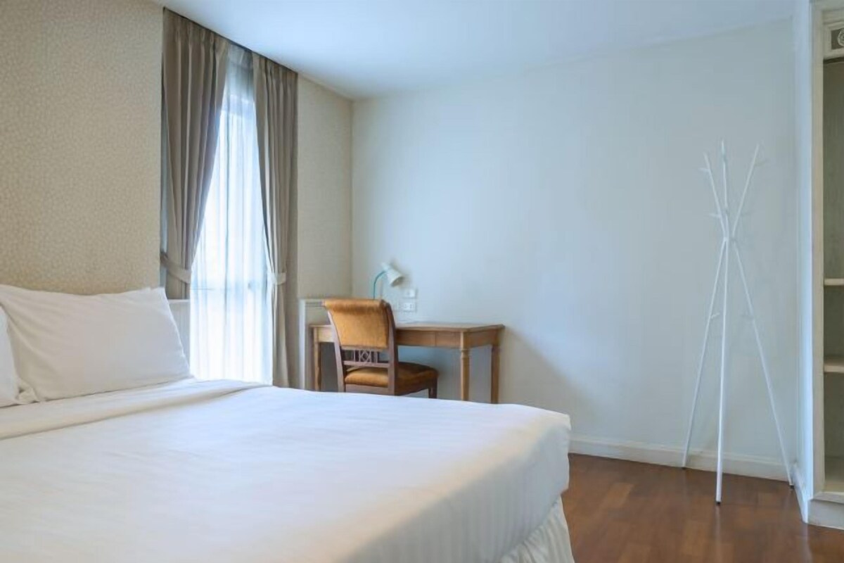 A hotel room with a large bed, a desk, and a chair.