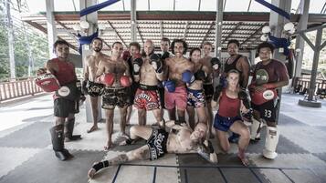 A group of people in a covered outdoor area with a roof, mats on the floor, and boxing gloves.