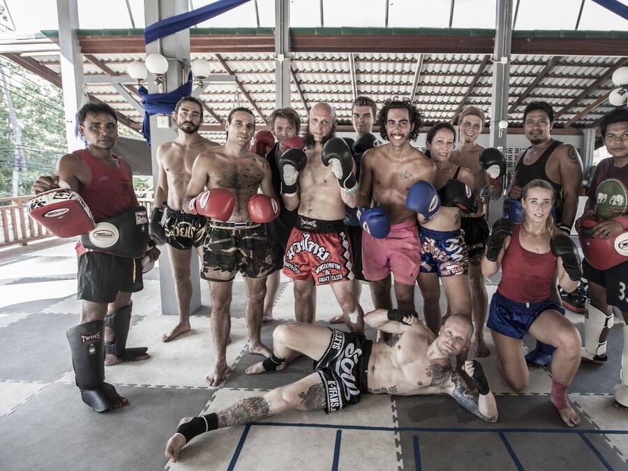 A group of people in a covered outdoor area with a roof, mats on the floor, and boxing gloves.