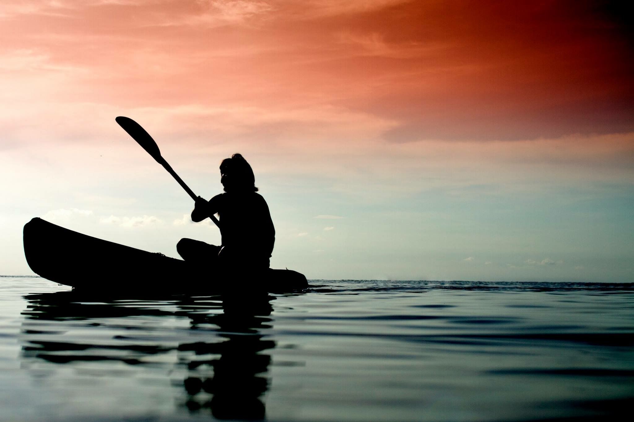 A silhouette of a person kayaking on calm water during sunset.