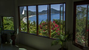 A room with large windows offering a view of a beach and ocean. - Monkey Flower Villas (Koh Tao)