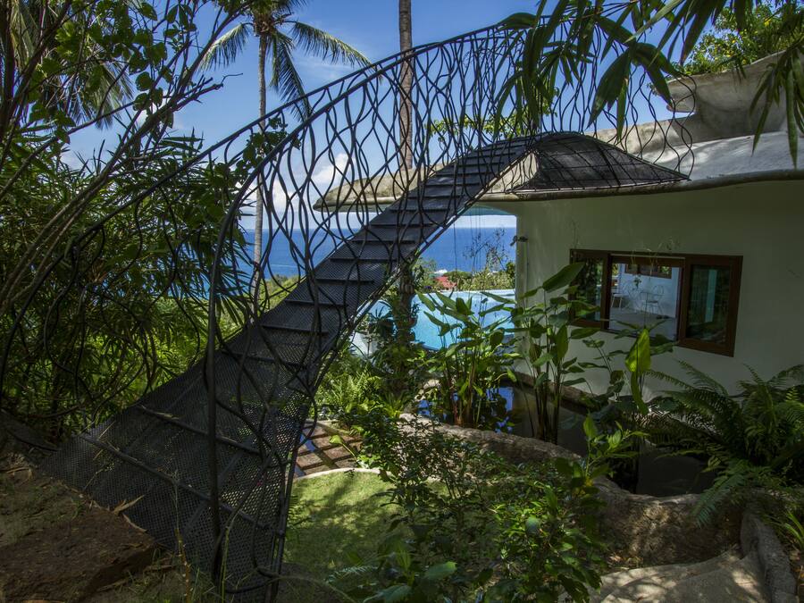 A staircase leading to a house with a view of the ocean, surrounded by lush greenery.