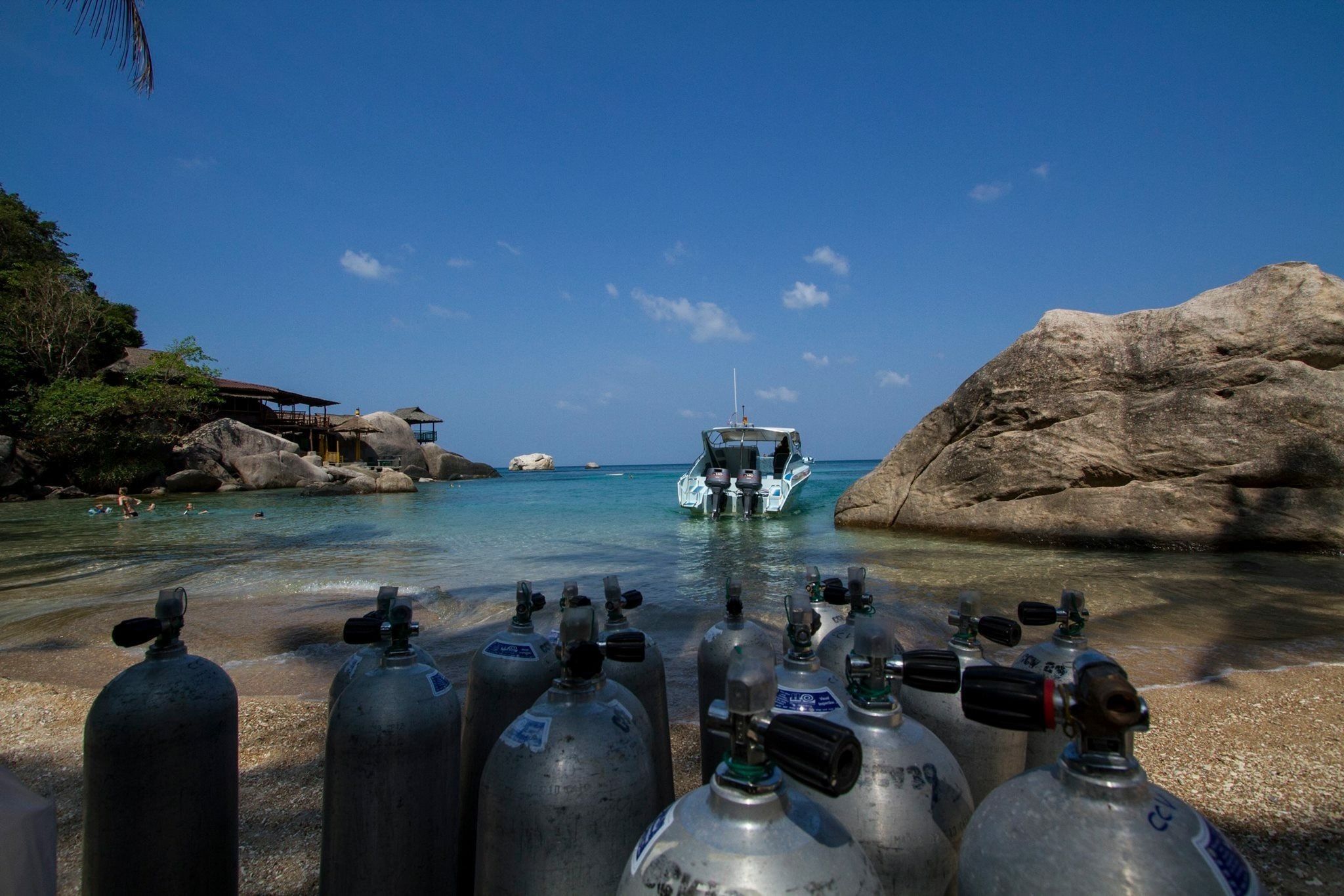 A beach with clear water, a boat, and several scuba diving tanks.