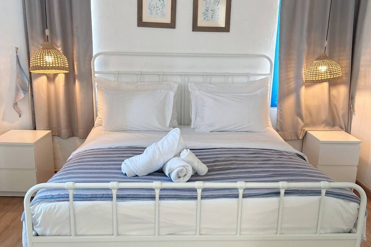 A bed with white bedding, two framed pictures on the wall, and two bedside lamps.