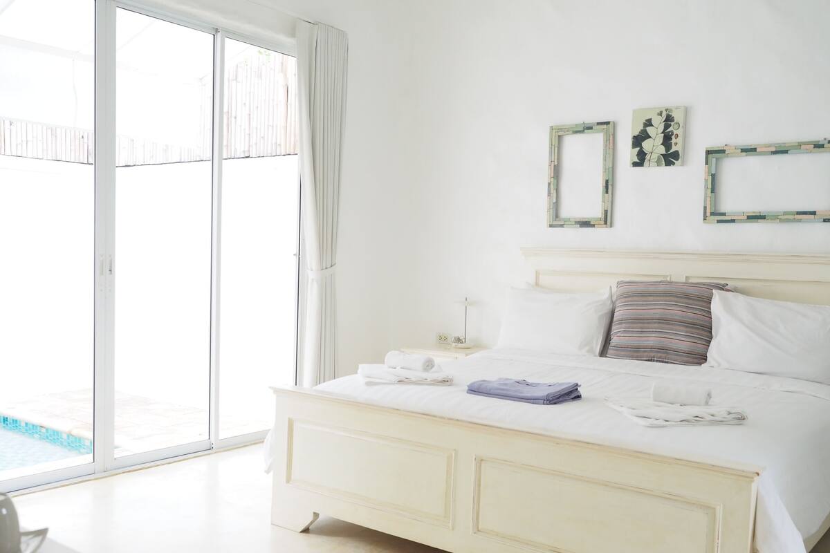 A bedroom with a bed, a nightstand, a lamp, and a view of a swimming pool.