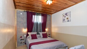 A bedroom with a wooden ceiling, a bed with a grey and red bedspread, a nightstand with a lamp, and a wall-mounted artwork. - L'Orky-Mel (Petite-Ile)