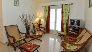A living room with a sofa, chairs, a TV, and a table with decorative items. - L'Orky-Mel (Petite-Ile)