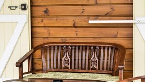 A wooden bench with a cushioned seat and backrest, a wooden table with a cup, and a hanging floral decoration. - L'Orky-Mel (Petite-Ile)