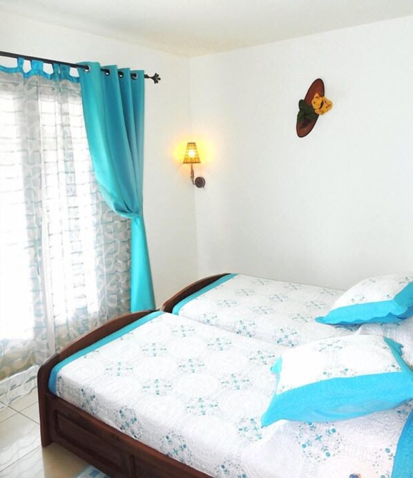 A bedroom with two beds, a window with curtains, a wall-mounted lamp, and a butterfly decoration.