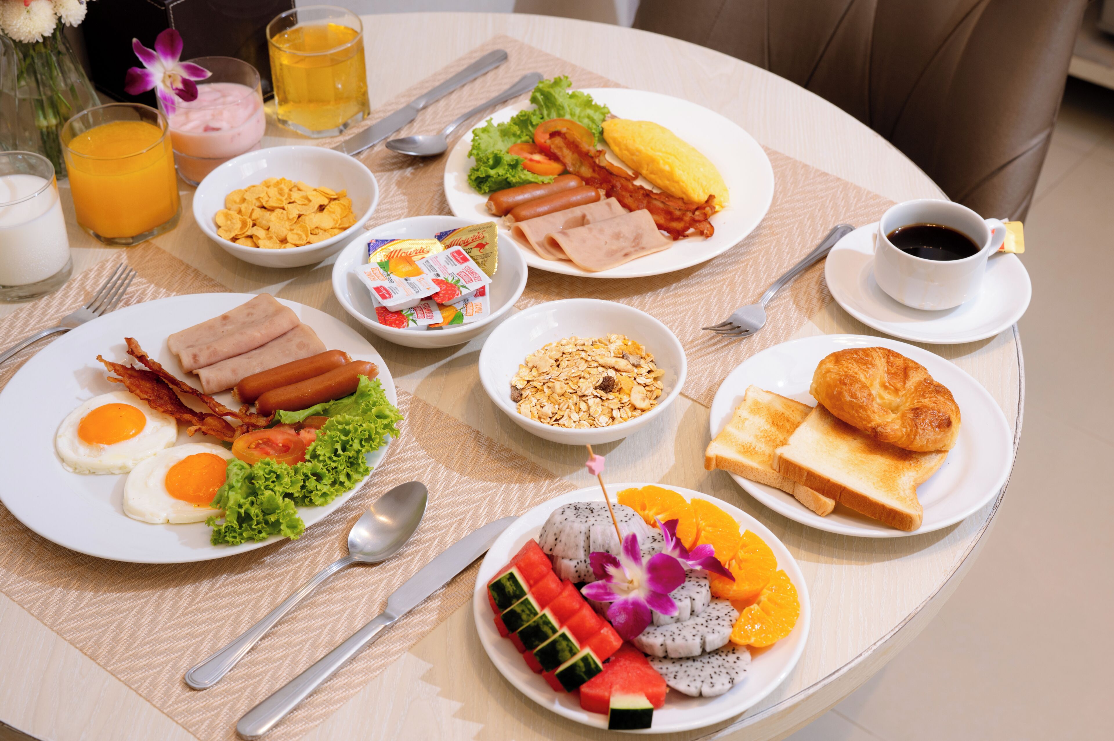 A breakfast table with plates of food, a cup of coffee, and a glass of orange juice.