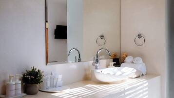 A modern bathroom with a large mirror, a round sink, and toiletries on the counter.