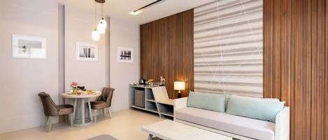A modern living room with a sofa, dining table, and chairs, a small kitchenette, and a wall with a striped pattern.