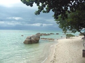 A beach with clear turquoise water, large rocks, and a tree-lined path.