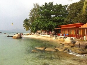 A beachside resort with a clear view of the ocean, large rocks, and a building with a red roof.